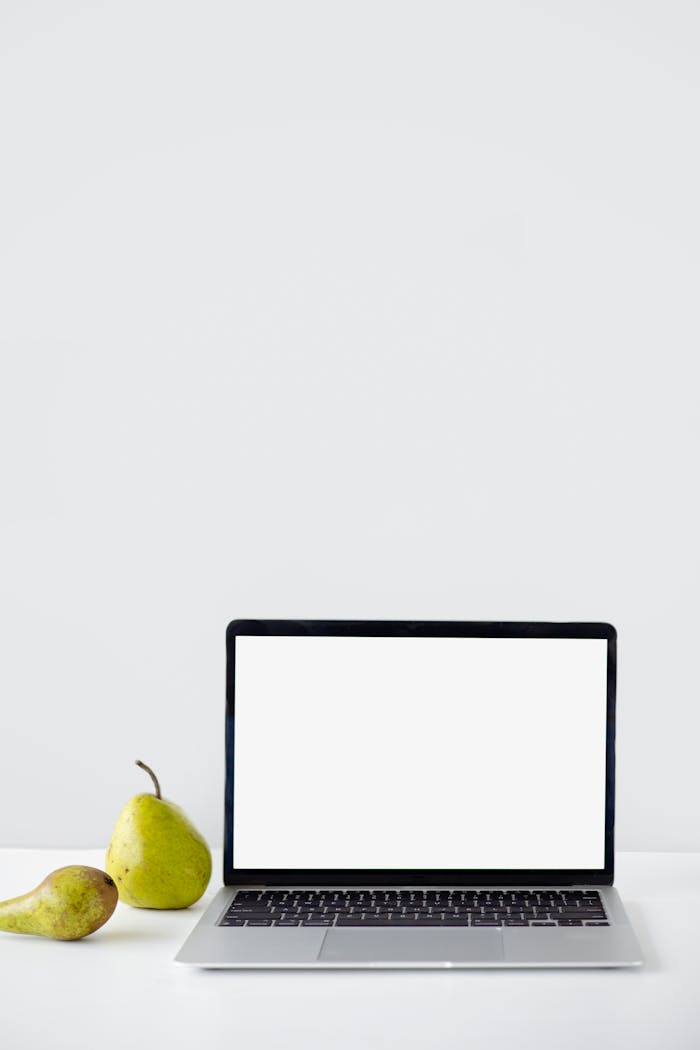 A minimalist setup with a laptop displaying a blank screen beside two pears on a white table.